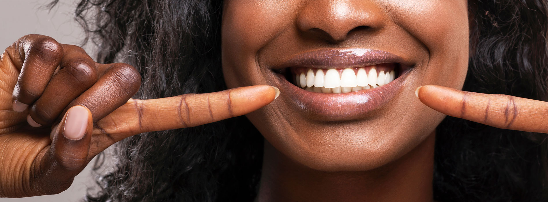 The image is a photograph of a woman with light skin, smiling at the camera. She appears to be in her late twenties or early thirties and has long hair. Her eyes are looking directly at the camera, and she is holding up her index finger near her mouth as if she s making a point or emphasizing something. The background is plain and light-colored, which suggests that this could be a stock photo used for various purposes such as advertising, personal branding, or lifestyle content.