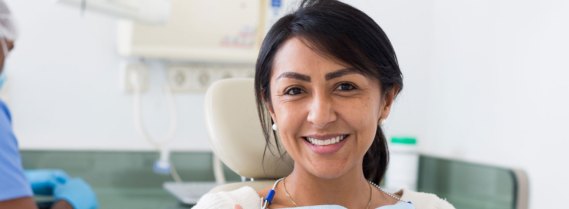 A person is seated in a dental chair, receiving care from a dental professional who stands behind them.
